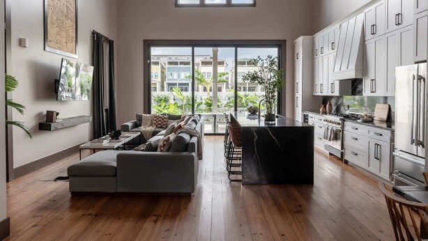 A modern living room with a sofa, a dining area, and a kitchen with white cabinets and stainless steel appliances. - The 1300 | 4 Home Combo, 28 bedrooms | Heated Pool (New Orleans)