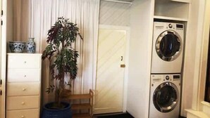 A compact laundry room with a washing machine and dryer, a potted plant, and a small wooden bench.