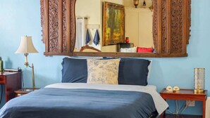 A bedroom with a large ornate mirror above a bed, a red chair, a nightstand with a lamp, and a patterned rug.