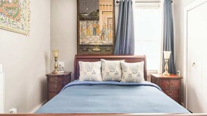 A bedroom with a wooden bed, a nightstand with a lamp, a painting on the wall, and a window with curtains. - Serene Private Suite Patio ~ Upscale Berkeley (Berkeley)