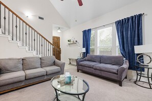 A living room with two sofas, a glass coffee table, a staircase, and a window with curtains. - Spacious 5-BD/3-BA Forest View Getaway (Sleeps 13) (Dallas)