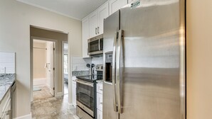 A modern kitchen with stainless steel appliances, white cabinets, and a marble countertop.