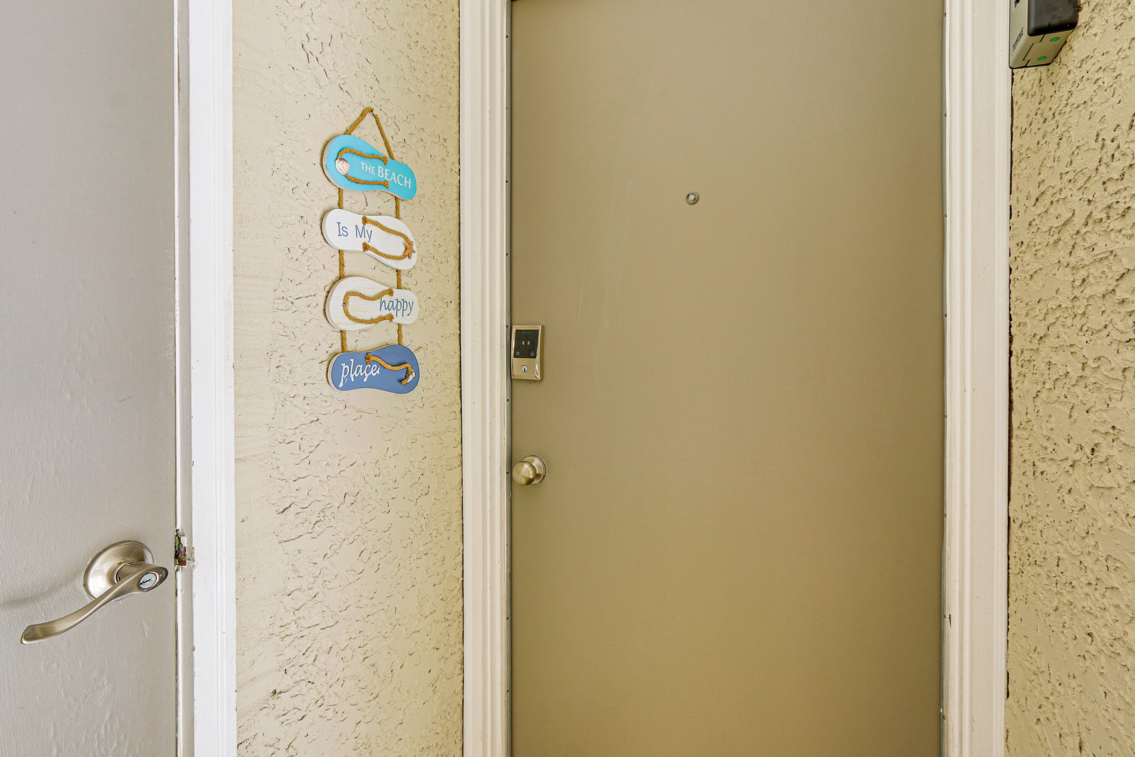 A beige door with a small electronic lock and a wall-mounted sign with the words "The Beach" and "Is My Happy Place."