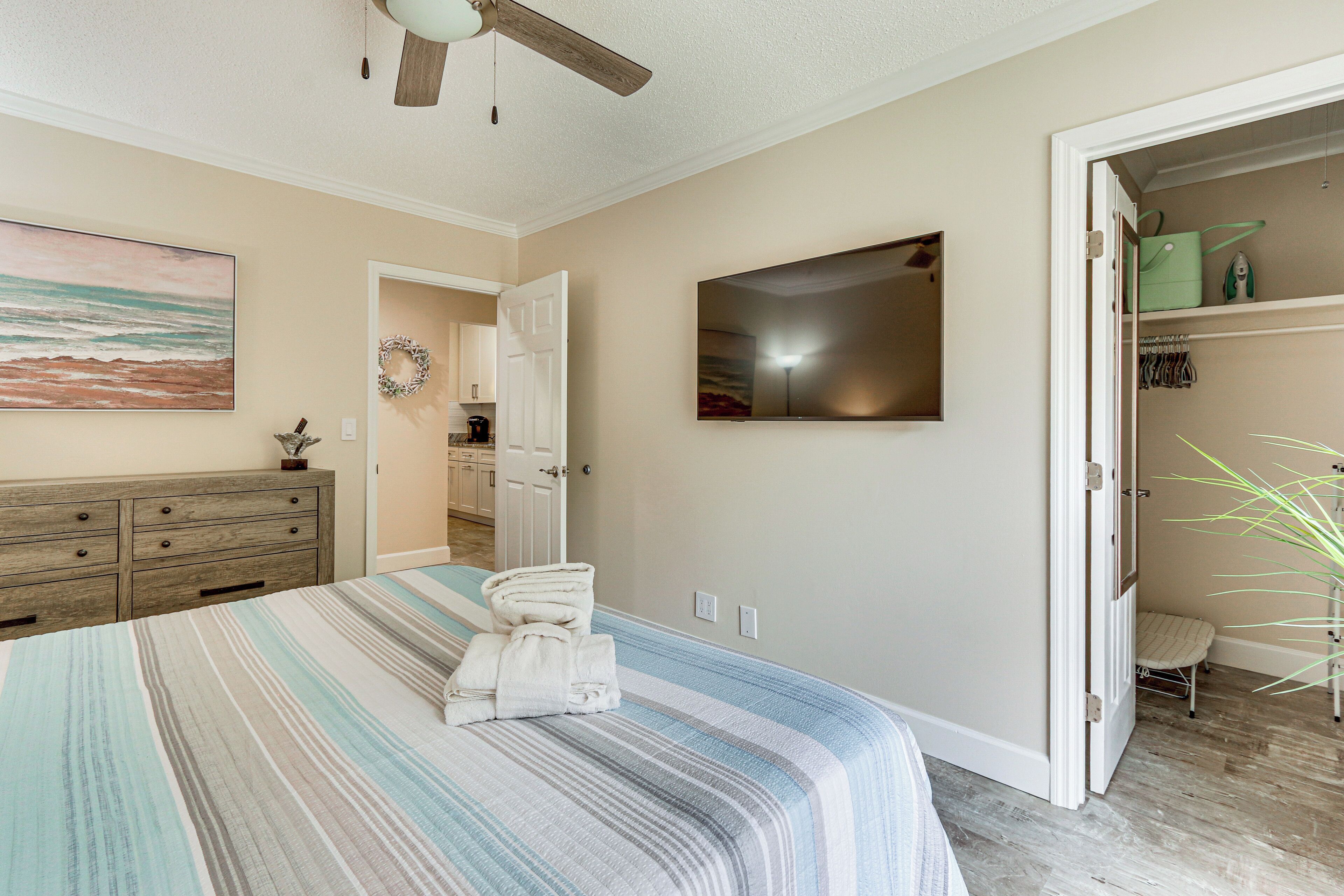 A bedroom with a bed, a ceiling fan, a wardrobe, a mirror, and a door leading to a closet.