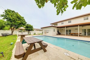 Un pati amb piscina, taula de picnic de fusta i zona de seients coberta.
