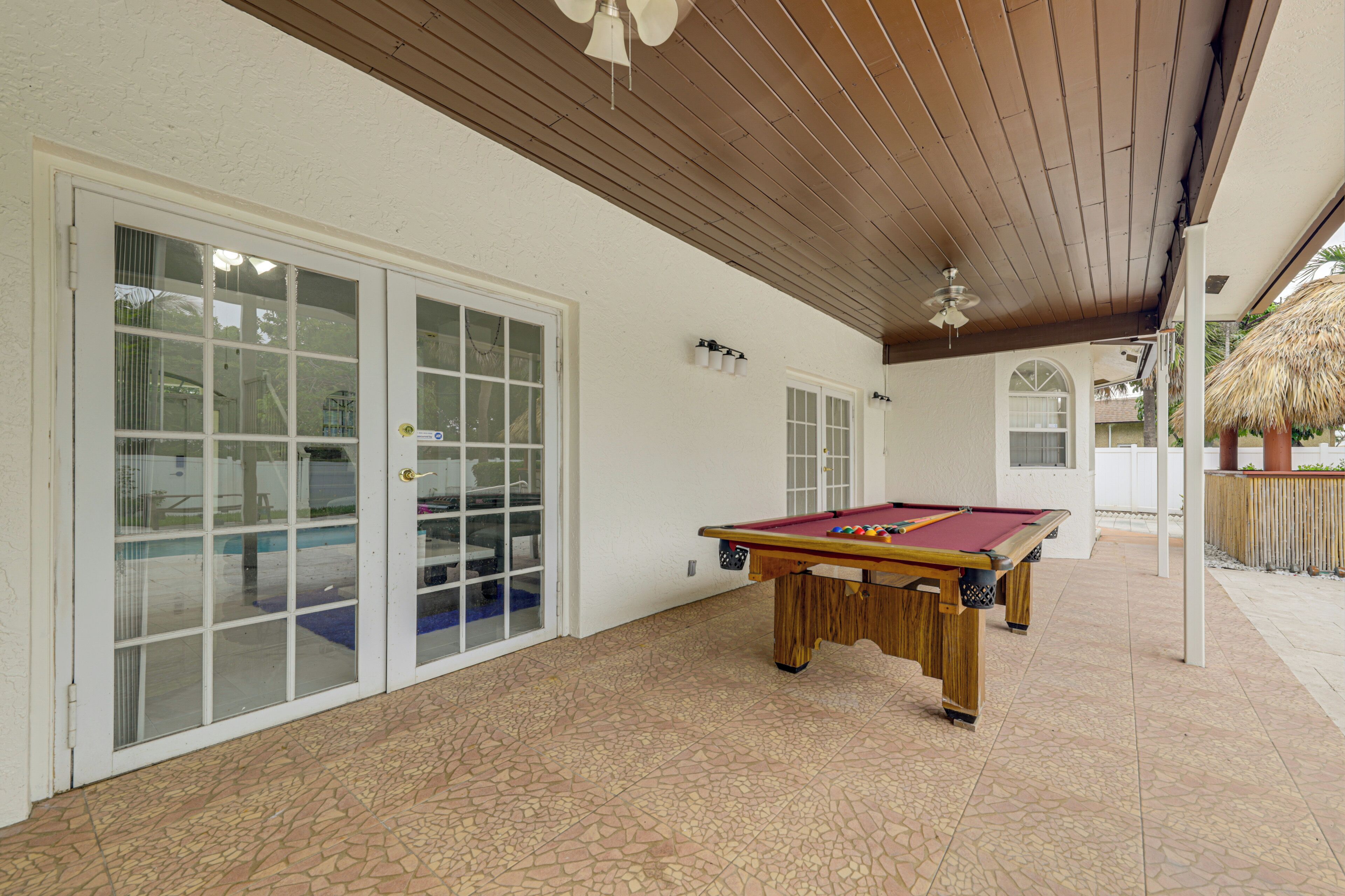 A pool table in a covered outdoor area with a tiled floor and a ceiling fan.