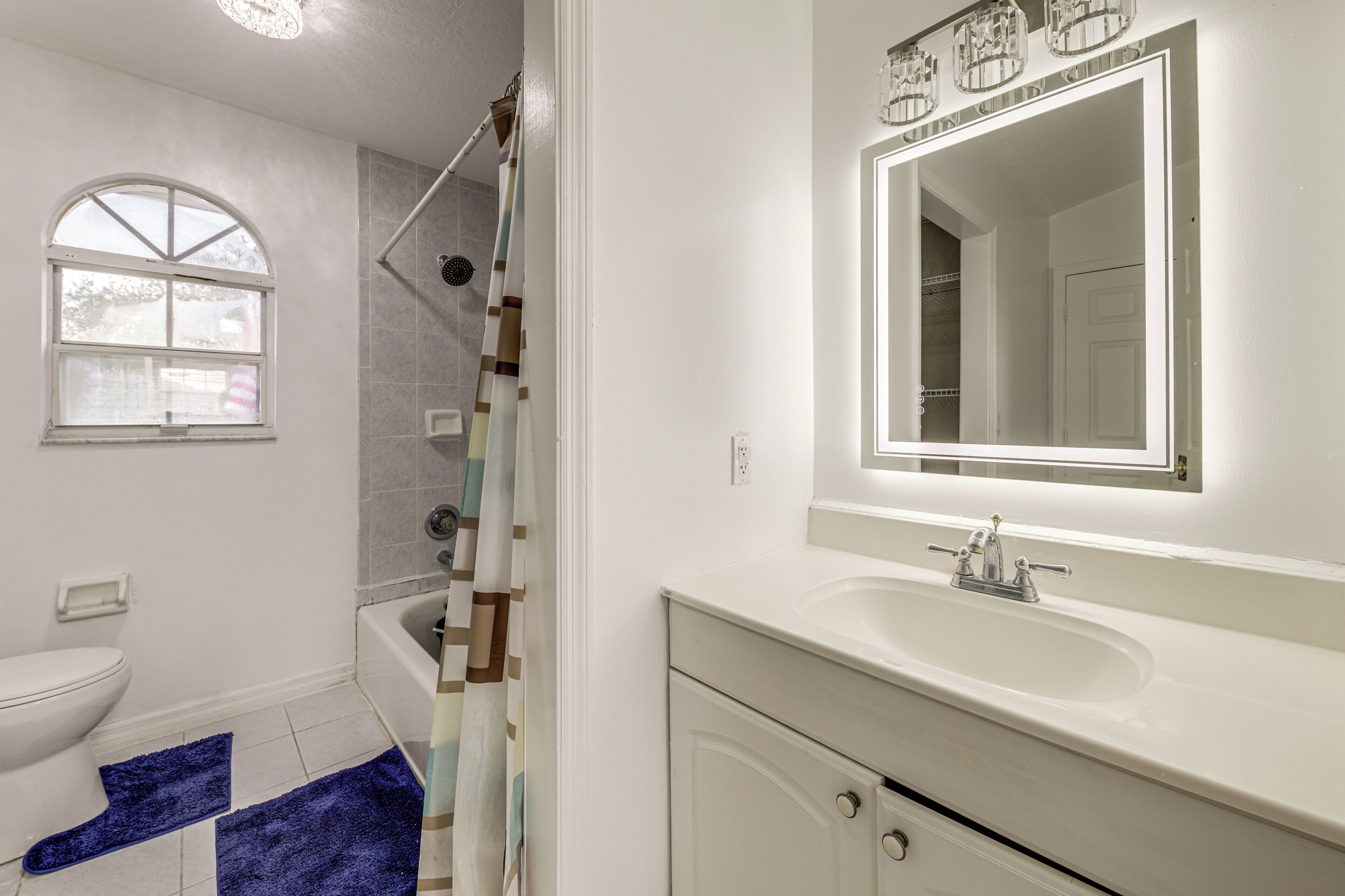Une salle de bain avec un lavabo blanc, un miroir, une douche et une fenêtre.