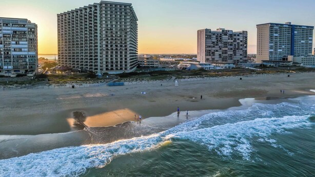 Un paisaje urbano costero con rascacielos, una playa arenosa y olas acercándose a la orilla.