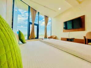 A hotel room with a large bed, a TV mounted on the wall, and a view of the sky through the window. - Hotel Galaxy (Banswara)