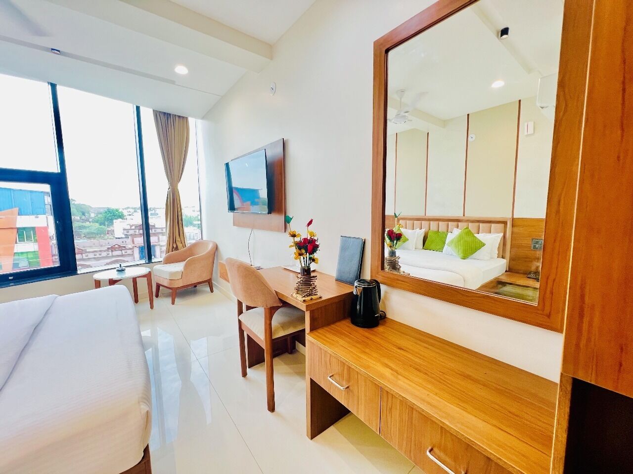 A hotel room with a bed, a desk, a chair, a TV, and a large mirror.