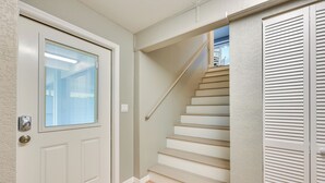 Un escalier avec une rampe, une porte avec une fenêtre et un carillon.