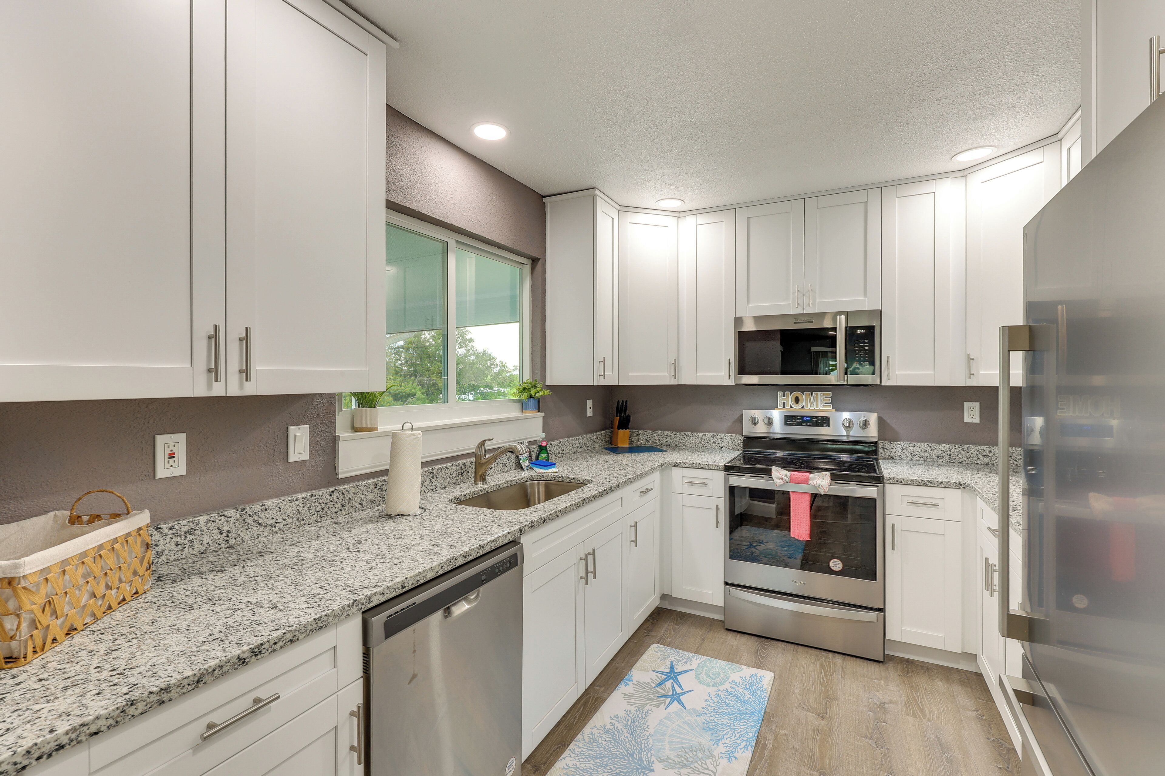 A modern kitchen with white cabinets, stainless steel appliances, a granite countertop, and a window with a view of greenery.