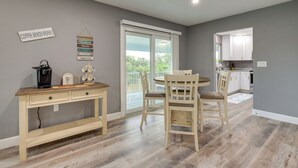 Une cuisine moderne avec des meubles blancs, un coin repas avec une table et des chaises en bois, et un espace dédié au café avec une machine à café et des tasses.