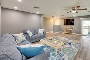 Un salon avec un canapé gris, une table basse en verre et un tapis orné d’un motif en forme d’étoile de mer.