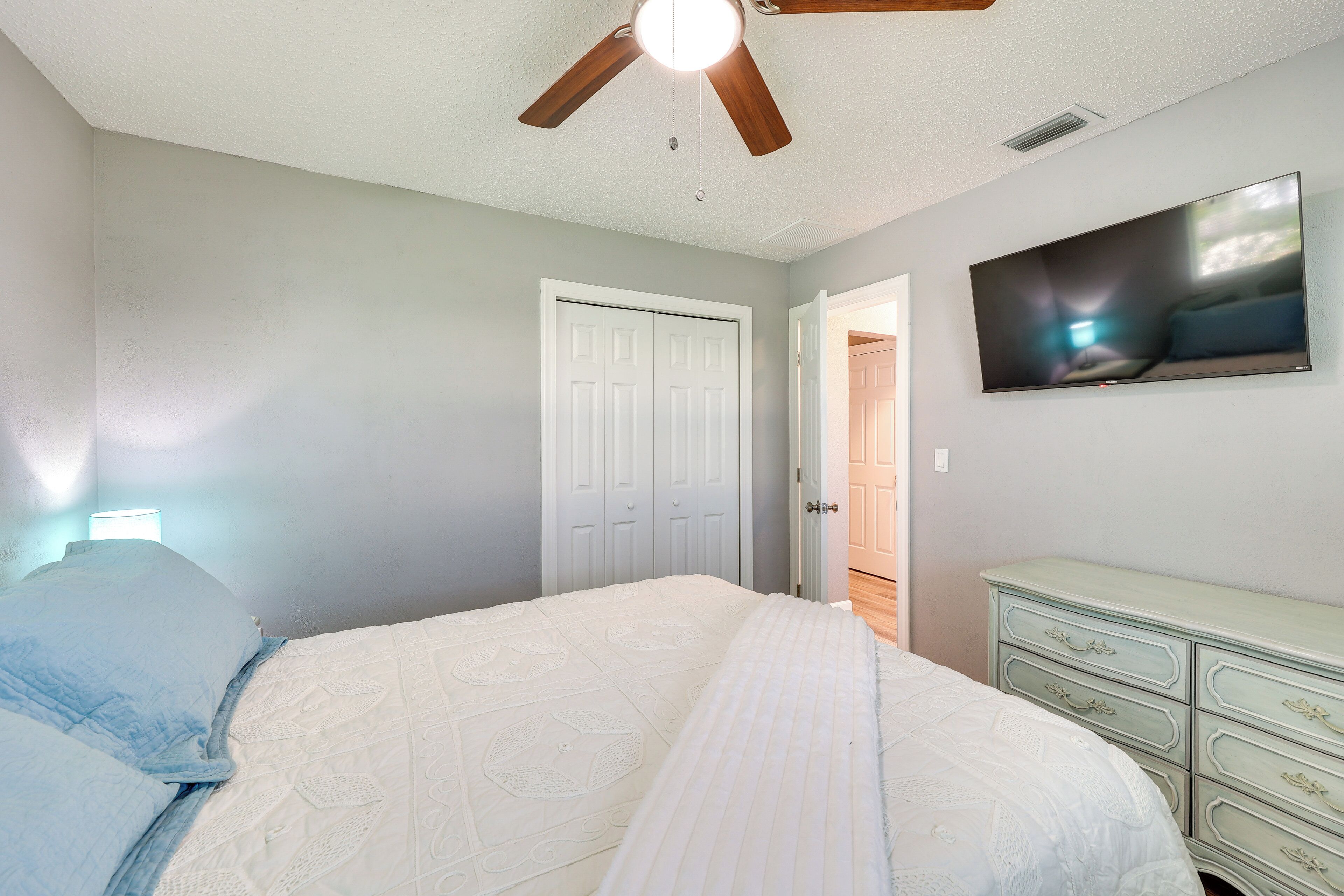 A bedroom with a bed, a ceiling fan, a dresser, and a TV on the wall.