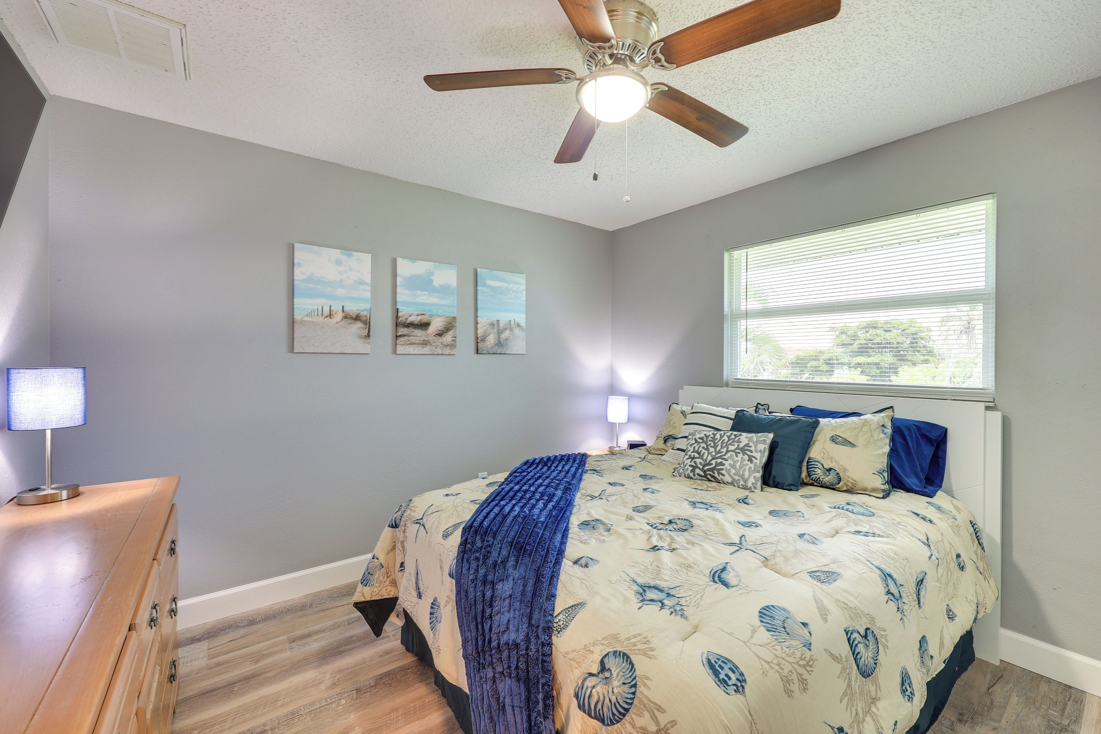 A bedroom with a bed, a ceiling fan, a dresser, and a window with blinds.
