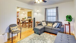 A living room with a grey sectional sofa, a grey armchair, a dining area with a table and chairs, and a ceiling fan.