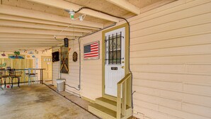 A covered outdoor area with a concrete floor, wooden steps leading to a door with an American flag, and a small trash can.