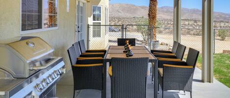An outdoor patio with a grill, wicker chairs, and a view of mountains.