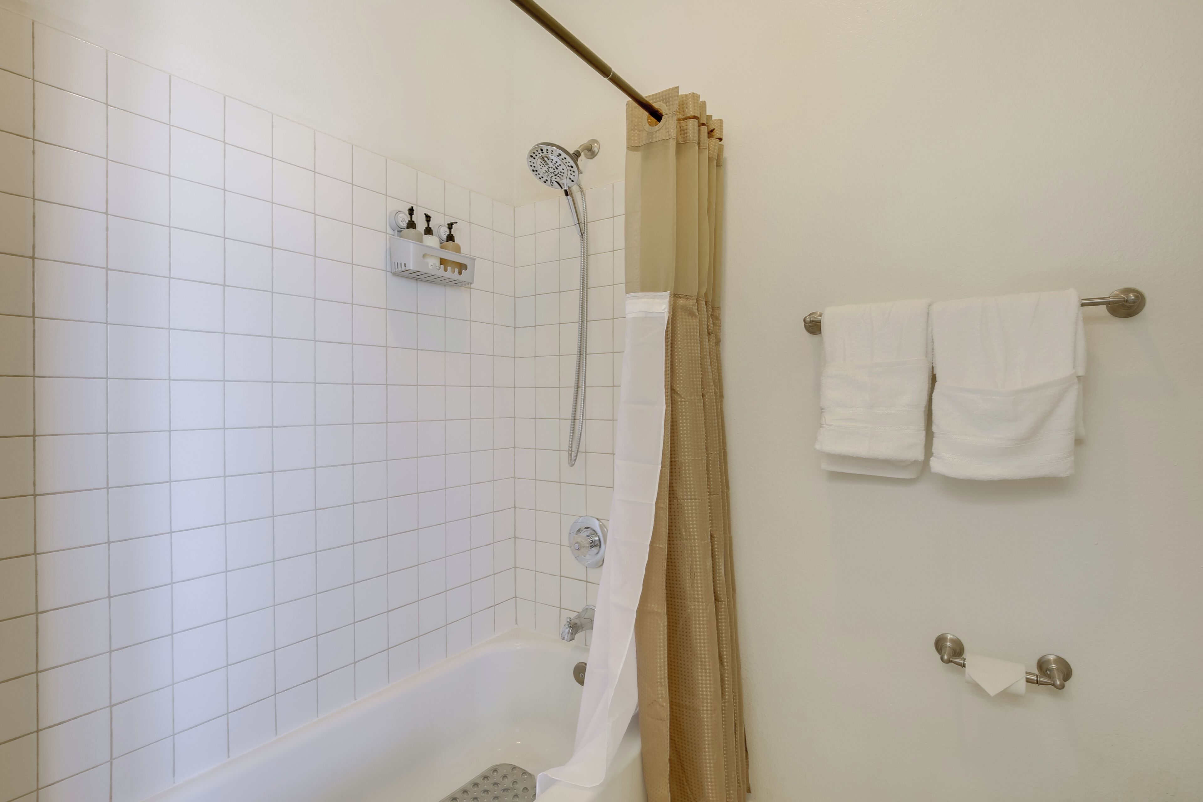 A bathroom with a bathtub, a showerhead, a towel rack with towels, and a toilet paper holder.
