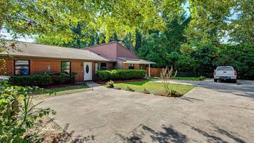 A two-story brick house with a front porch, a driveway, and a white car parked in the driveway.