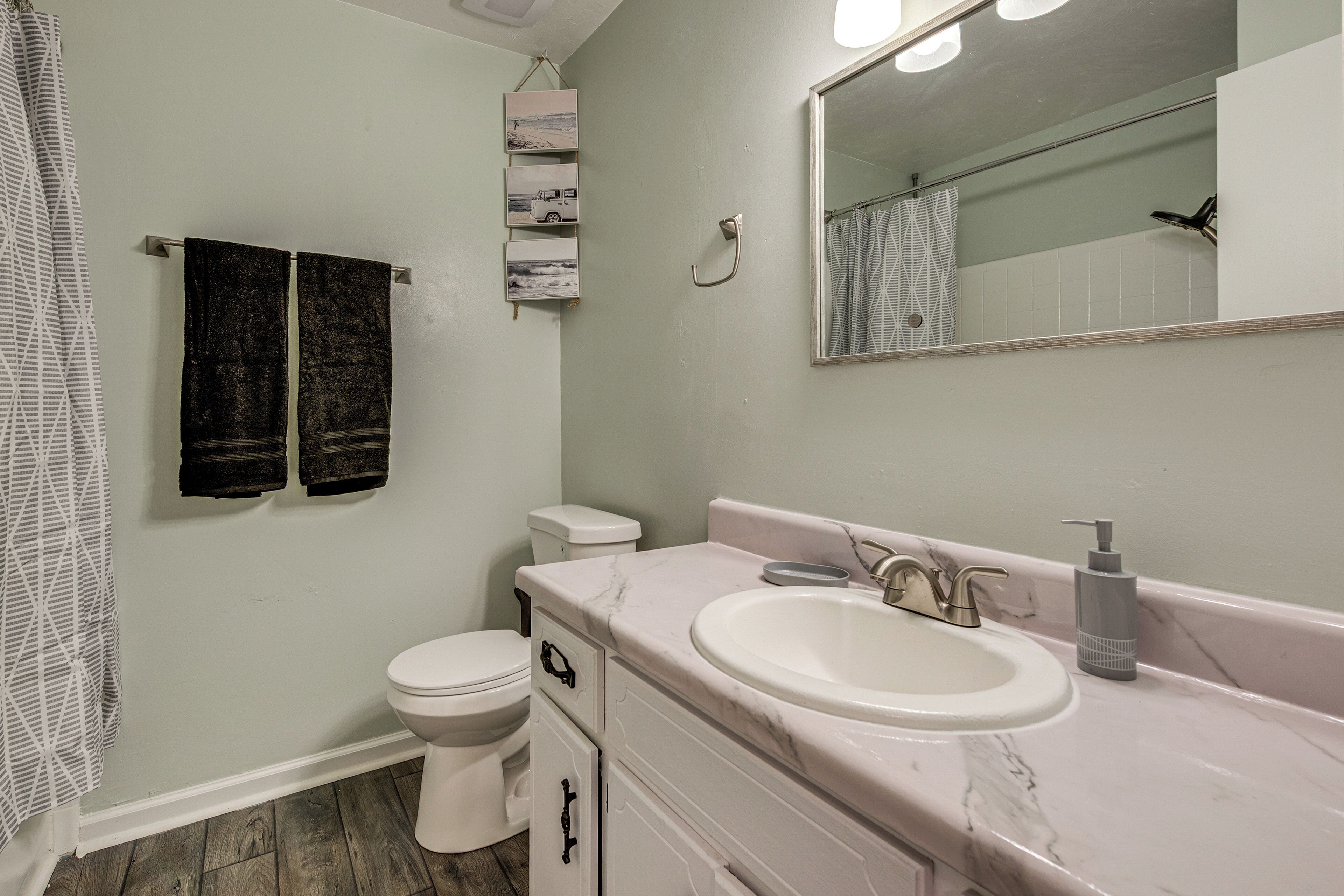 A bathroom with a white toilet, a sink with a marble countertop, a shower curtain, and a mirror.