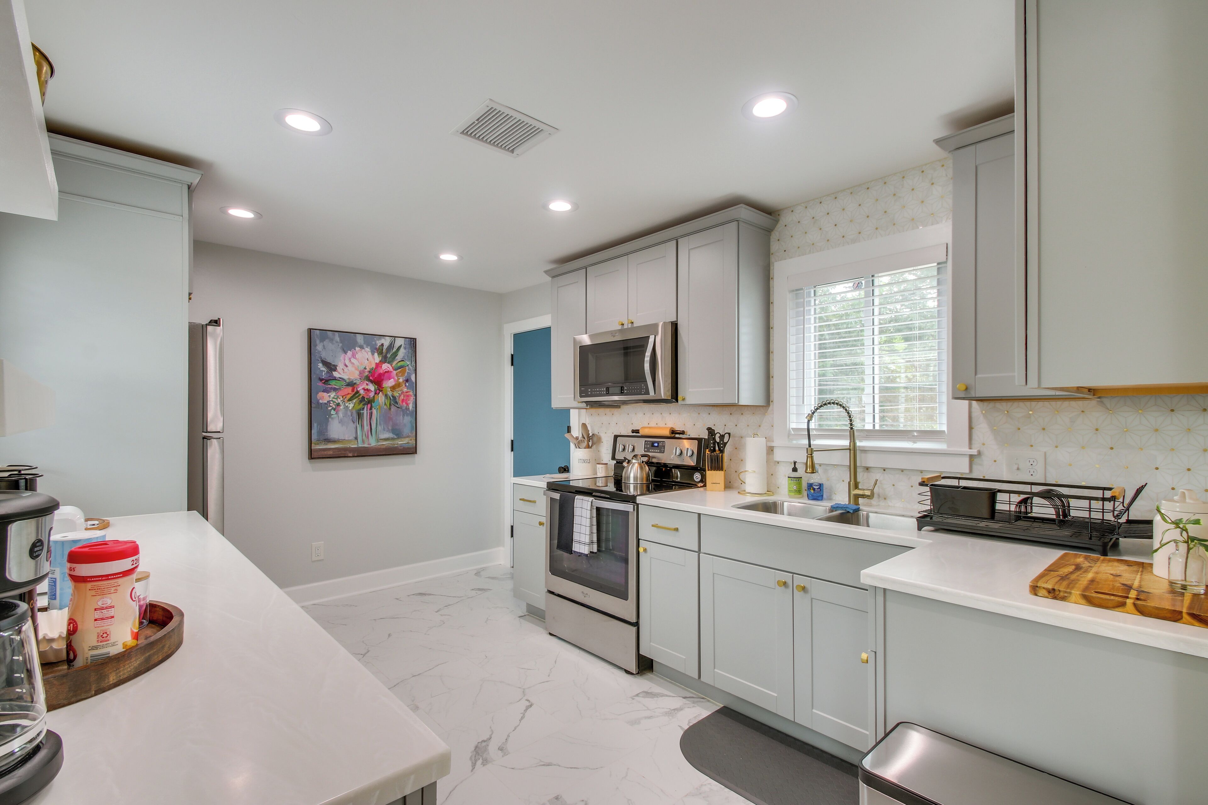A modern kitchen with white cabinets, stainless steel appliances, and a marble floor.