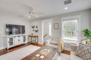 Una sala de estar con televisión, mueble blanco, sofá y mesa de centro, además de un ventanal grande.