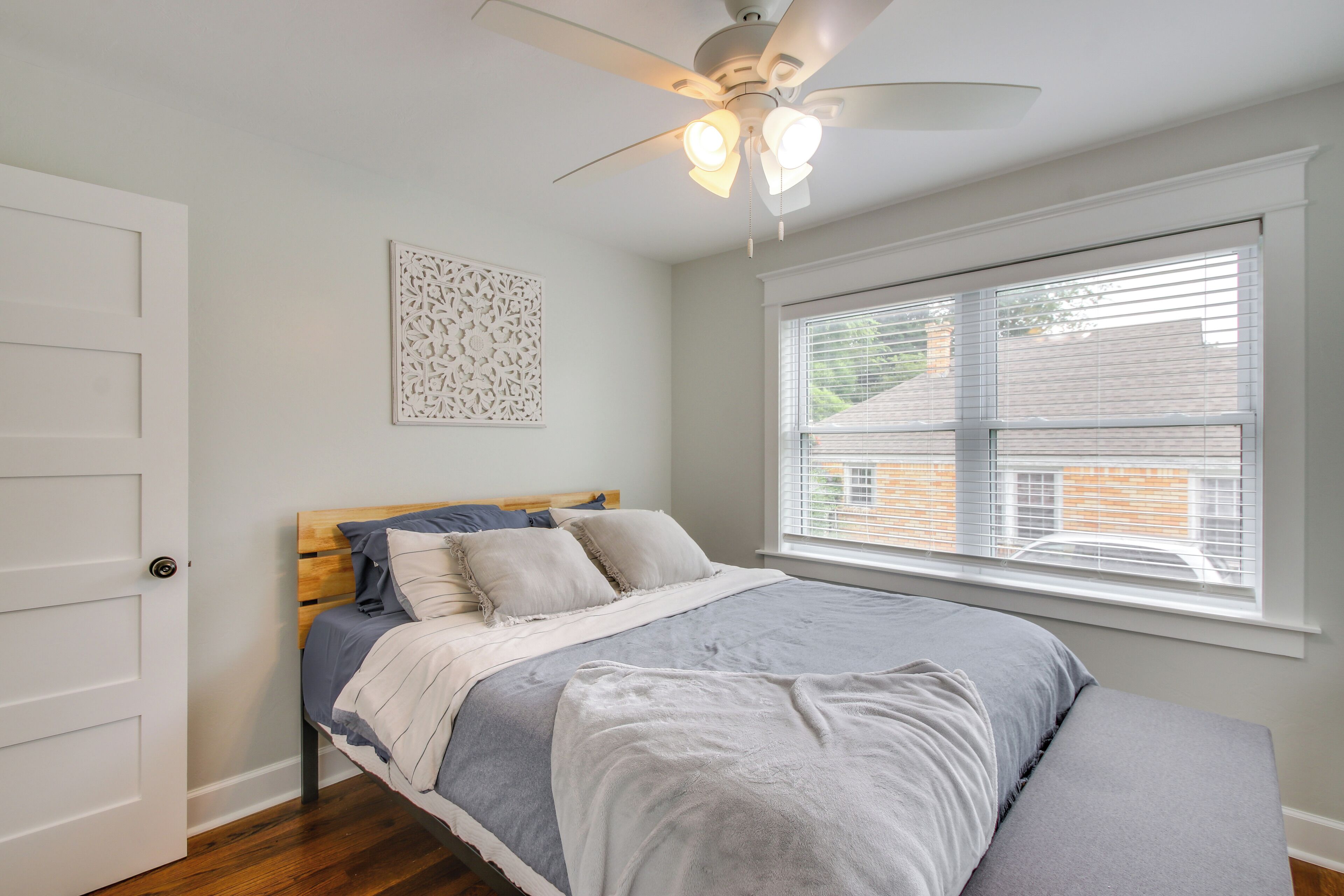 A bedroom with a bed, a ceiling fan, a window with blinds, and a door.