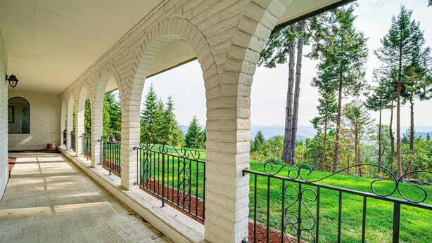 A covered outdoor area with stone arches, a metal railing, and a view of a green landscape with trees. - Mtn Views & Hot Tub: Umpqua Valley Villa! (Roseburg)