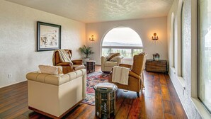 A spacious living room with a large arched window, a fireplace, and a cozy seating area. - Mtn Views & Hot Tub: Umpqua Valley Villa! (Roseburg)