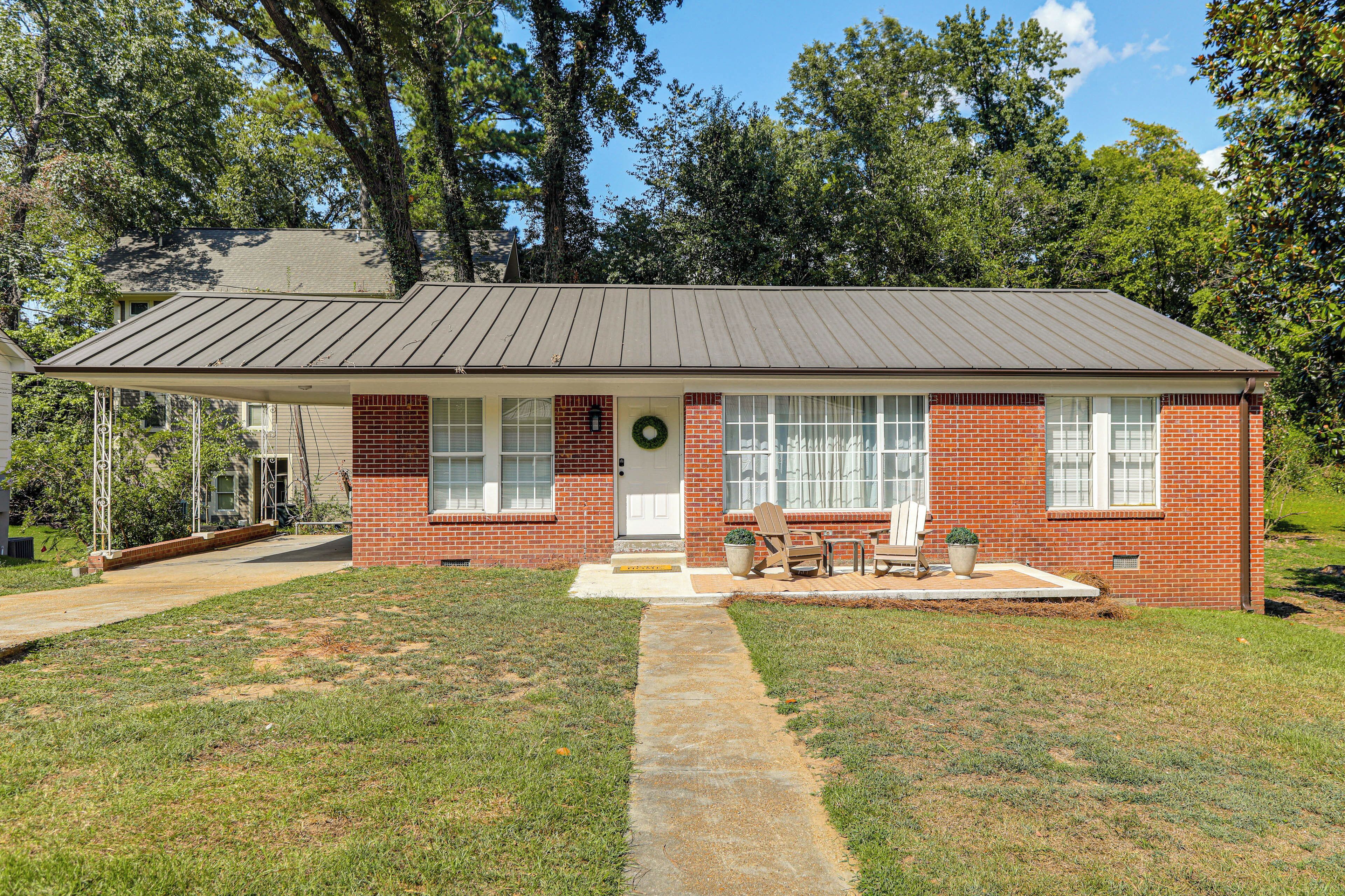 A single-story brick house with a front porch, a small garden, and a clear sky.