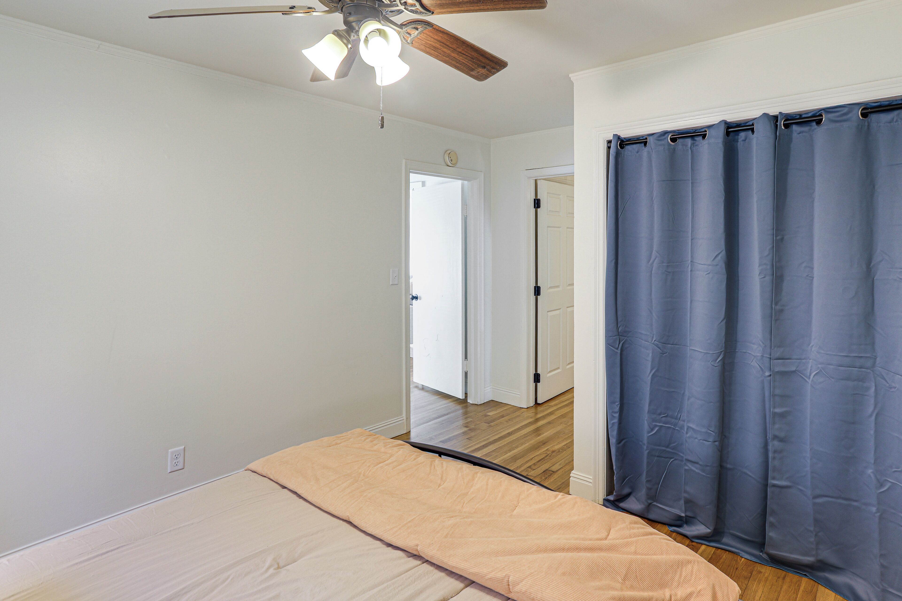 A bedroom with a bed, ceiling fan, and a door leading to another room.