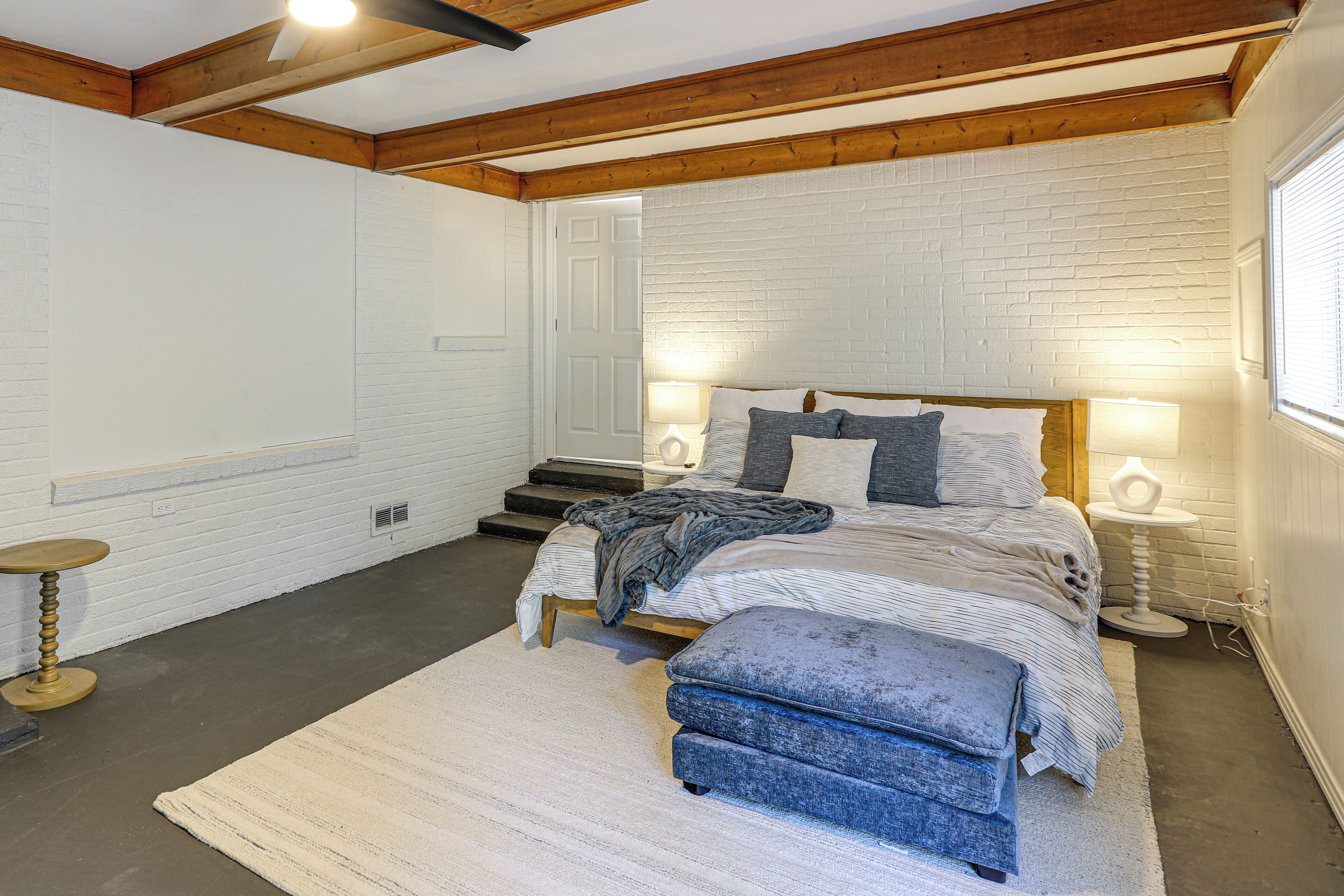 Un dormitorio con cama, lámparas de noche, un banco y una puerta.