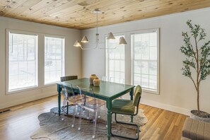 Een eetgedeelte met een groene tafel, transparante stoelen en een kroonluchter.