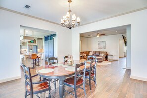 Un comedor amplio con una gran mesa de madera y sillas, una araña, y vistas a la cocina y la sala de estar.