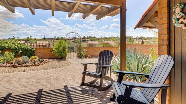 A covered patio with two Adirondack chairs, a brick pathway, and a view of a distant building with a curved roof. - Quiet Townhome w/ Mountain Views in Green Valley (Green Valley)