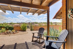 A covered patio with two Adirondack chairs, a brick pathway, and a view of a distant building with a curved roof. - Quiet Townhome w/ Mountain Views in Green Valley (Green Valley)