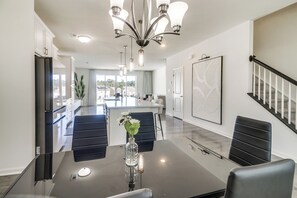 Een moderne keuken met een centraal eiland, donkere stoelen en een eettafel met een bloevas.