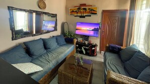 A living room with a sofa, a coffee table, a TV, and a door. - Cool 1-bedroom with a balcony in vibrant Kigali (Kigali)