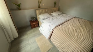 A bedroom with a bed, bedside tables, a nightstand, and decorative plants. - Cool 1-bedroom with a balcony in vibrant Kigali (Kigali)
