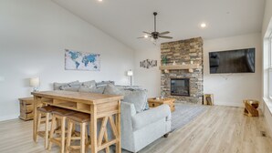 A modern living room with a wooden dining table, grey sofa, and a stone fireplace.