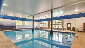 An indoor swimming pool with clear blue water, a lifeguard stand, and a mural of mountains on the wall.