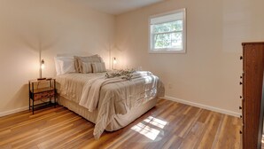 A bedroom with a wooden floor, a bed with a beige comforter, a bedside table with a lamp, and a window with blinds. - 16 Mi to Lake Sara Beach - Pet-friendly Home (Montrose)