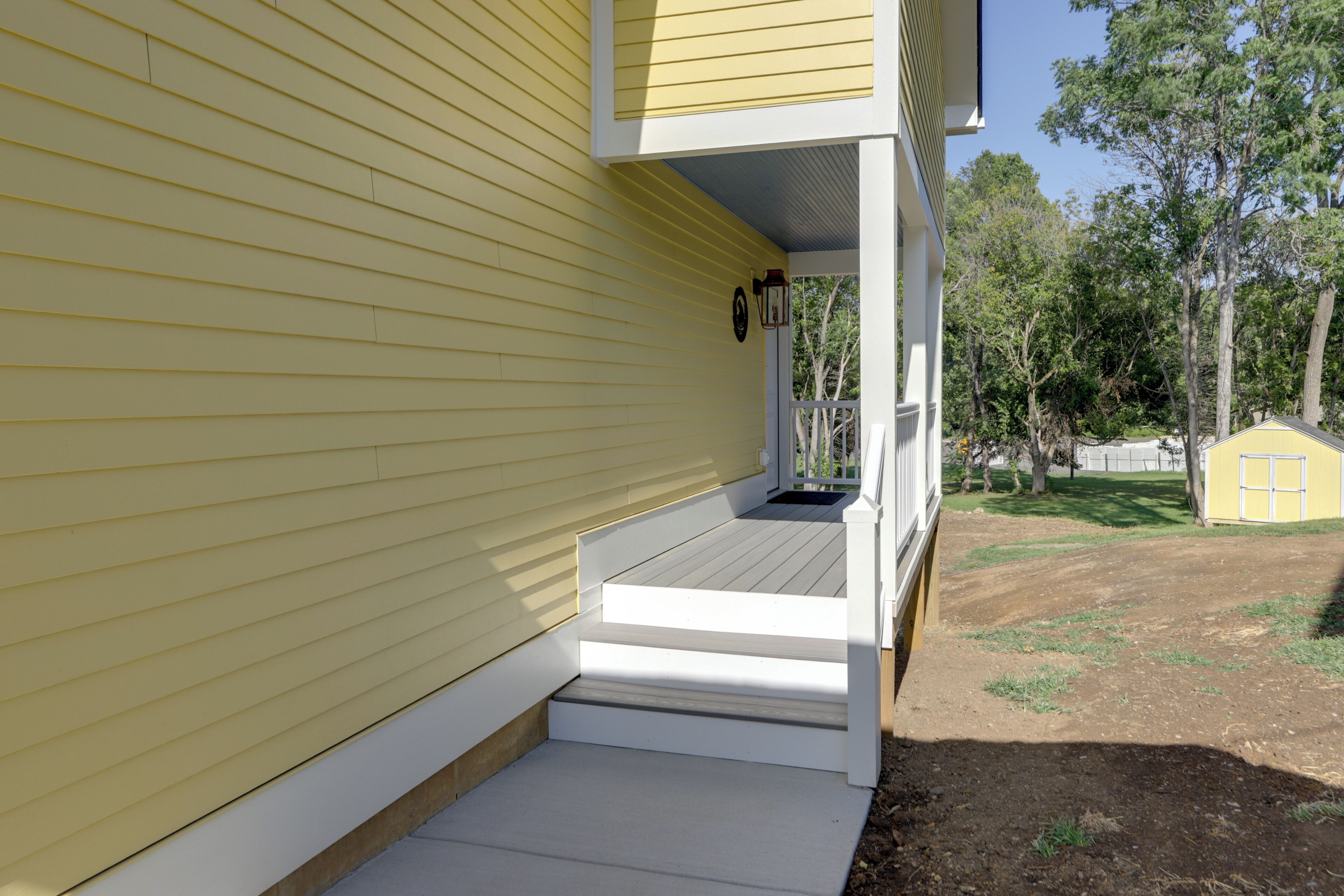 A yellow house with a white porch and steps leading to a door.
