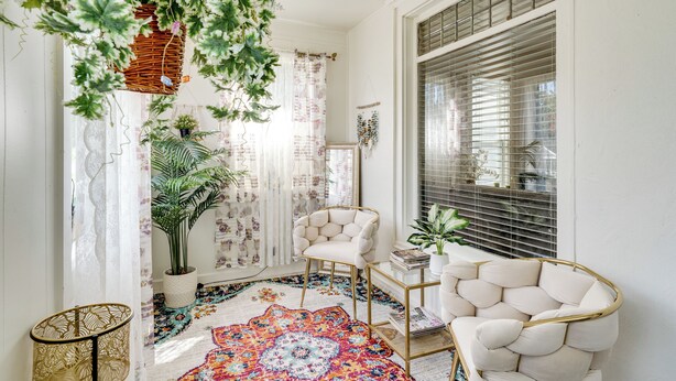 Een gezellige kamer met een kamerbreed tapijt, een witte fauteuil, een klein tafeltje en een potplant.