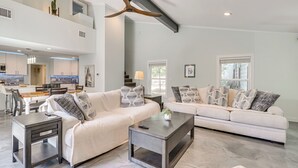 Ein geräumiges Wohnzimmer mit hohen Decken, eine moderne Küche im Hintergrund und ein Essbereich.
