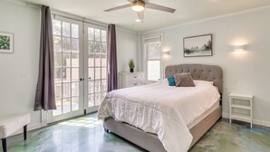 Ein Schlafzimmer mit Bett, Deckenventilator, einem Fenster mit Vorhängen und einer Tür, die zu einem Außenbereich führt.