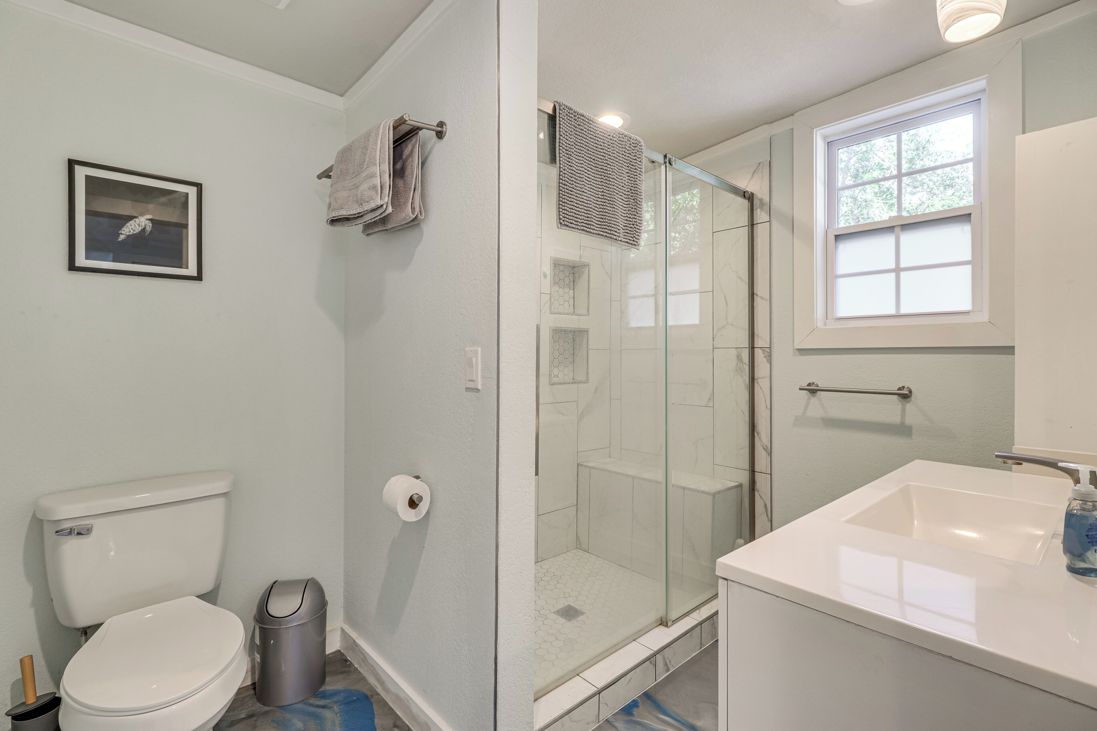 A bathroom with a toilet, a shower with a glass door, a sink, and a window.