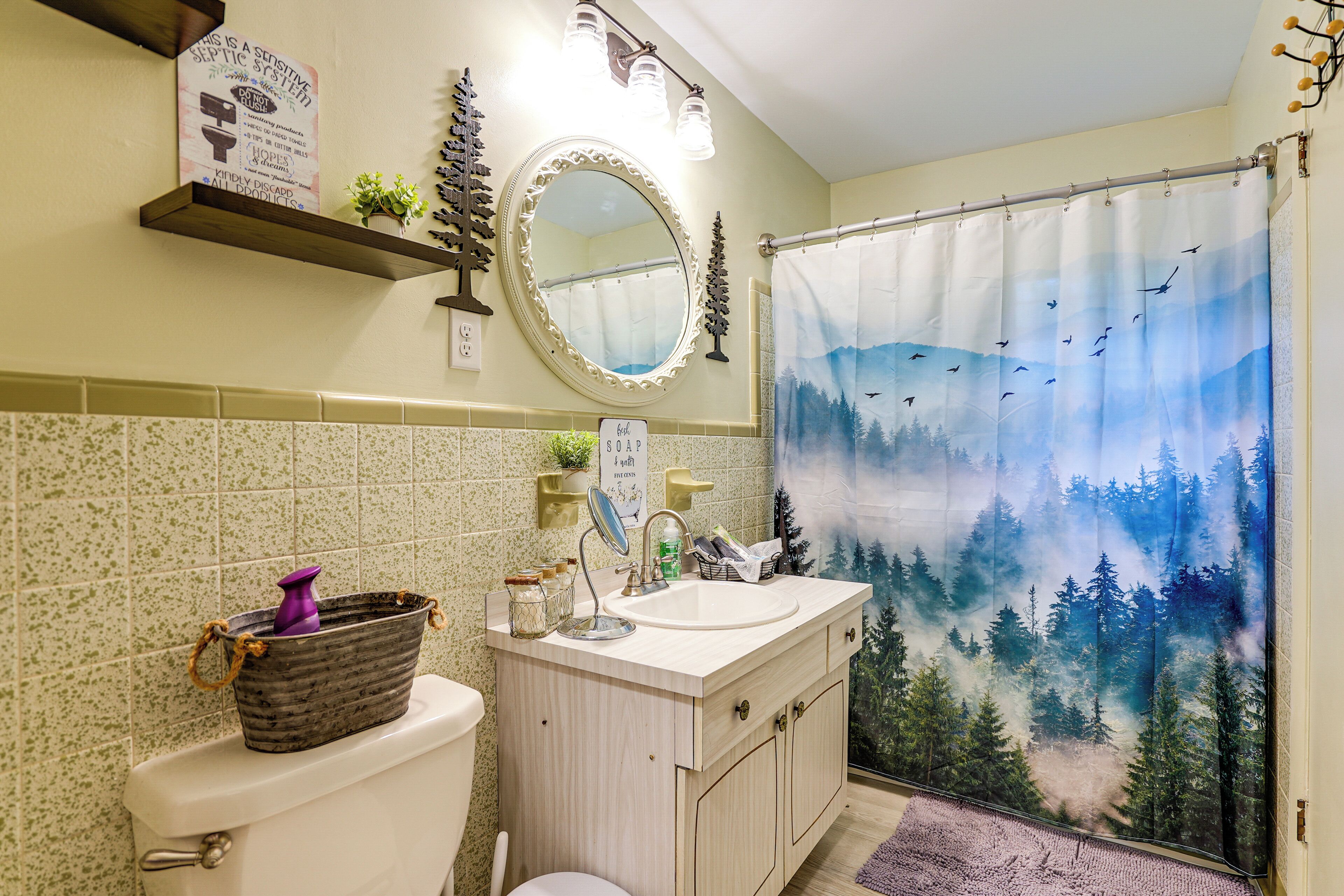 A bathroom with a toilet, sink, mirror, and shower curtain with a forest scene.